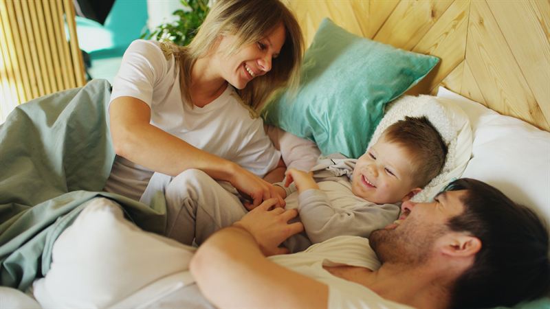 Pai, mãe e filho pequeno brincando juntos na cama pela manhã